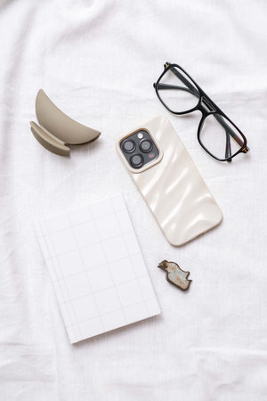 This is a stylish and trendy flat lay featuring a smartphone and glasses against a soft backgroundの写真素材