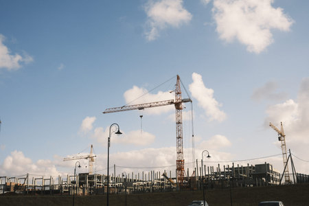 A bustling construction site features cranes silhouetted against a vibrant blue sky