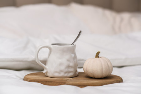 A warm mug of rich cocoa with a small pumpkin creates a cozy autumn vibe in a charming bedroom atmosphereの写真素材