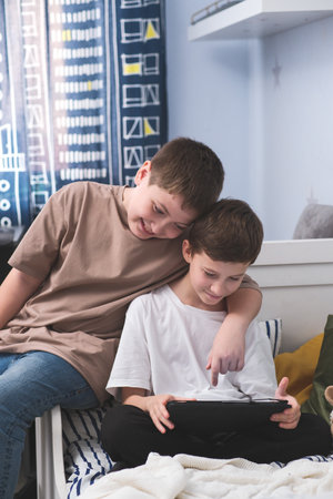 Boys enjoy various tablet activities together in a cozy bedroom, having a great timeの写真素材