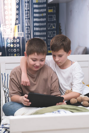 Boys enjoy various tablet activities together in a cozy bedroom, having a great timeの写真素材