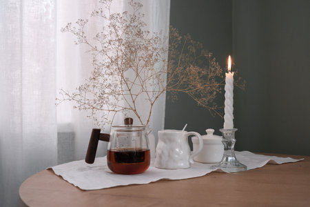A Cozy Tea Setup Featuring a Beautiful Candle and Delicate Dried Flowers for Ambianceの写真素材