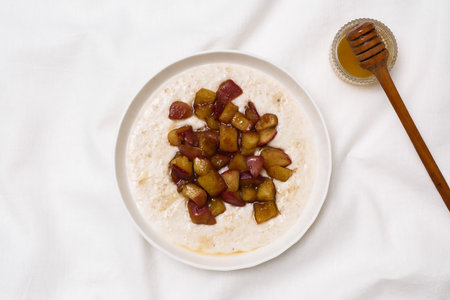 A warm bowl of oatmeal topped with caramelized apples, perfect for a cozy breakfast on white fabric background.の写真素材