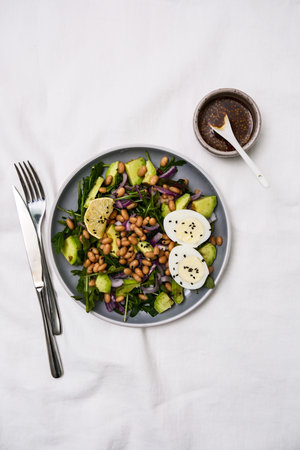 Colorful salad that brings together fresh greens, beans,assorted vegetables, avocado, egg, lemon and sauce on white background.の写真素材
