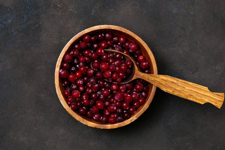 A beautifully arranged bowl filled with vibrant red cranberries, set against a rich dark brown...