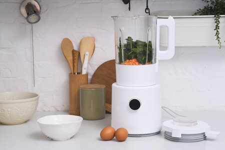 A beautifully stylish kitchen scene showcases a modern blender surrounded by vibrant fresh vegetables and eggsの写真素材
