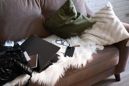 A Stylish and Functional Workspace Featuring a Laptop, mobile phone, notebook with glasses, books in bag on sofa.の写真素材