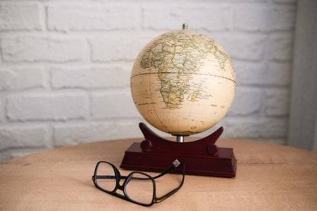 An exquisite Vintage Globe paired with elegant Glasses resting on a beautifully Wooden Table.
