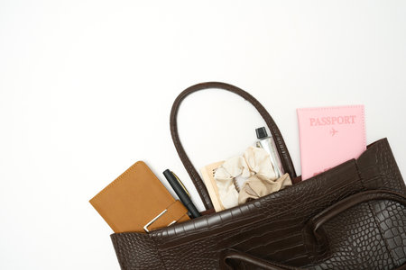 Top view of woman brown bag open out with accessories passport, notebook, cosmetics, perfume on white background.の写真素材
