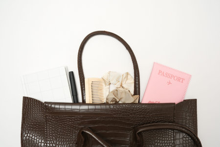 Top view of woman brown bag open out with accessories passport, notebook, cosmetics, perfume on...
