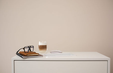 A serene workspace with a latte, notebooks, and stylish glasses on white table.