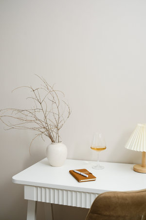 A beautifully minimalist table with white wine drink, a notebook, and an elegant decorative vase on white wooden table.の写真素材