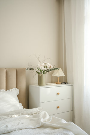 A serene bedroom with a stylish bed, plush pillows, and fresh flowers on white dresser artfully arranged in the room.の写真素材