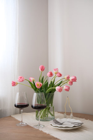 A beautiful bouquet of pink tulips beside a glasses of rich red wine, candles, plates enhance home decor and ambiance. Table serving.の写真素材