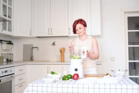 A woman makes a vibrant healthy smoothie with fresh fruits and greens, promoting a healthy lifestyle...