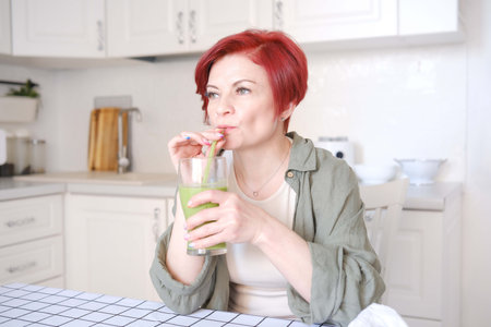 A woman is happily enjoying a healthy and refreshing green smoothie in her stylish and modern kitchen settingの写真素材
