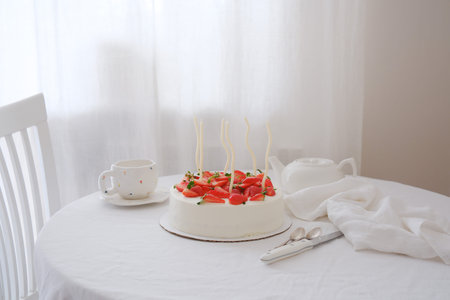 A delicious cake with fresh strawberries next to a charming tea set on the table