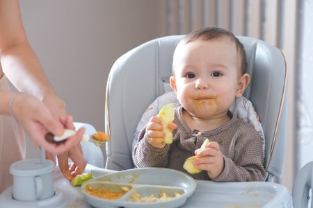 Mother feeding her baby son. Mother giving healthy food to her adorable child at homeの写真素材