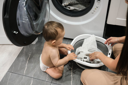 Cute baby boy with his mom near washing machine in laundry room, closeupの写真素材