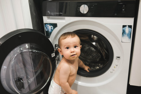 Cute toddler near washing machine in laundry room, closeupの写真素材
