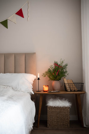 Christmas decor in interior. Fir branches in vase, candle, books in basket on wooden bench in bedroom.の写真素材