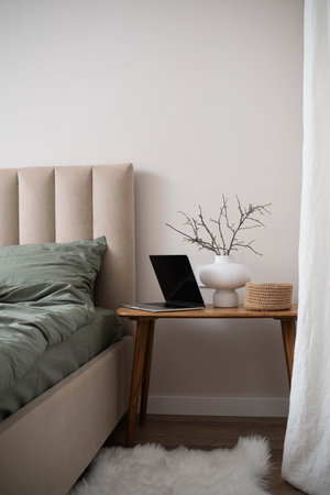 Autumn decor. Interior of stylish bedroom with comfortable workplace, wooden coffee table, notebook, vase with branches and green bed sheets.の写真素材