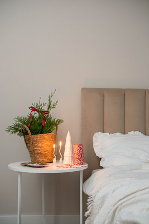 Cozy Christmas decor in a light and bright bedroom, bed, white bed sheets, fir branches in a straw...