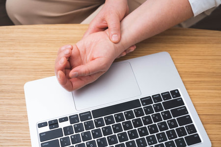 Close-up of a person holding their wrist in pain while working on a laptop. Concept of carpal tunnel...