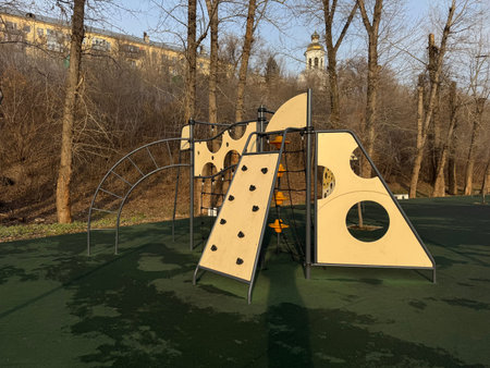 Modern outdoor playground with climbing structures and activity panels on a green rubber surface,...