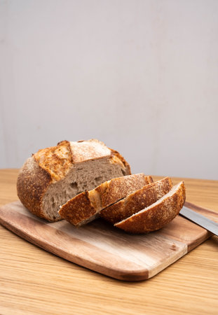 A rustic sourdough loaf on a wooden cutting board, partially sliced, with a wooden-handled knife...