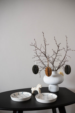 Minimalist table setting with a white textured vase holding bare branches adorned with paper eggs....