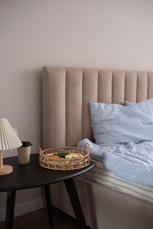 Cozy morning scene: bed with light blue striped bedding, beige upholstered headboard, side table...