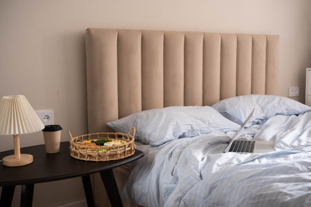 Cozy bed scene with light blue striped bedding, woven basket holding a plate of healthy breakfast...
