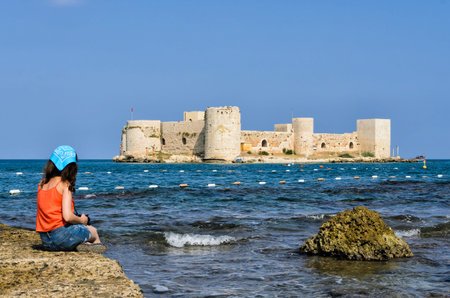 woman watching castle from beach mersin kizkalesi on the rock pier castle in the sea turkeyのeditorial素材