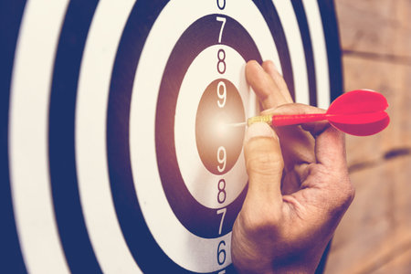 hand holding darts and stabbing or puncturing on dart board.Business target or goal success and winner the marketing concept.free space.の写真素材