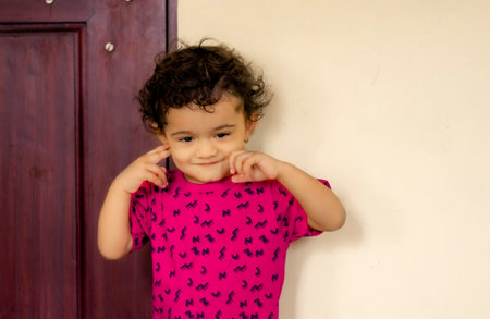 A small Hindu child stood inside the house by touching his soft cheeks with fingers and wearing a...