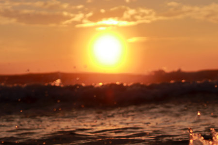 A defocused background in which a which bright round sun rises above the sky with the rising waves...