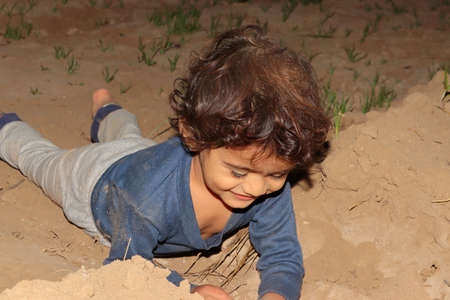 close-up of An Indian child playing with soil and laying on the ground in the field, concept to childhood.の写真素材