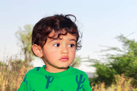 Close-up front view portrait of An Indian cute little cute male boy child posing outside and blur background of green nature outdoorsの写真素材