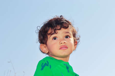 Low angle Close-up portrait of cute smart little Indian male child posing outside against background of clear skyの写真素材