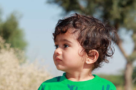 close-up profile view portrait of A small cute Indian Hindu child wearing a green shirt stands outside looking awayの写真素材