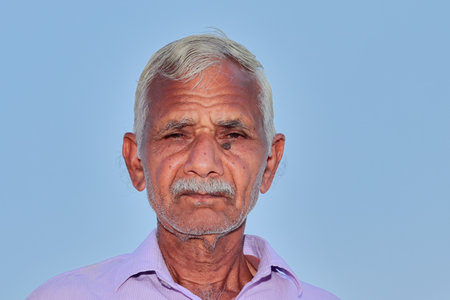 low angle shot of Close up face photo of elderly Indian Hindu farmer man with clear blue sky background behindの写真素材