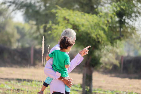 close-up of Indian-origin elderly grandfather lifting his younger grandson in the womb, showing a distant object in the field with a gesture of the handの写真素材