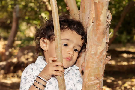 Close-up portrait of An Indian resident little hindu boy posing to think sadly and unhappy with laying head on tree trunkの写真素材