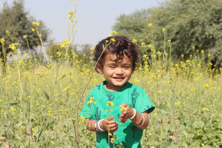Close-up portrait of A cute little boy standing in a mustard field smiling at the yellow flowers of the mustard crop to an Indian-origin farming familyの写真素材
