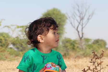 close-up profile view portrait A young male child from an Indian-origin farming family standing in the field and looking away with wearing green t-shirtの写真素材