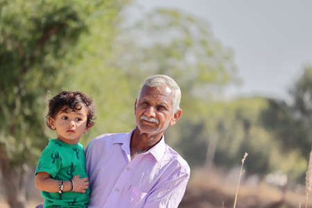 Close-up of portrait of A cute little boy from an Indian-origin farming family sits in his senior grandfather's womb, looking at the cameraの写真素材