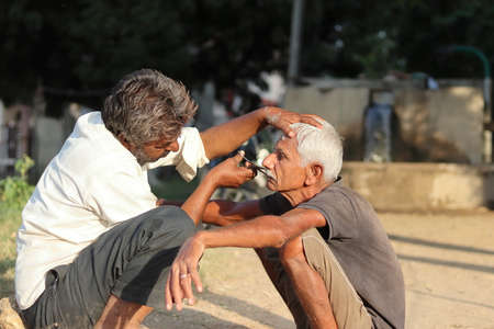 Pali Rajasthan, India - âNovember 1, â2021. An Indian barber cuts an old man's mustache with scissors in an open yard without shopのeditorial素材