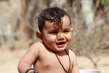 Close-up Photo of A small cute Indian Hindu baby looks at the camera while taking a bath with unclothedの写真素材