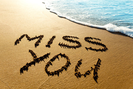 Dramatic inscription "Miss You" on wet golden beach sand in sunset lightの写真素材
